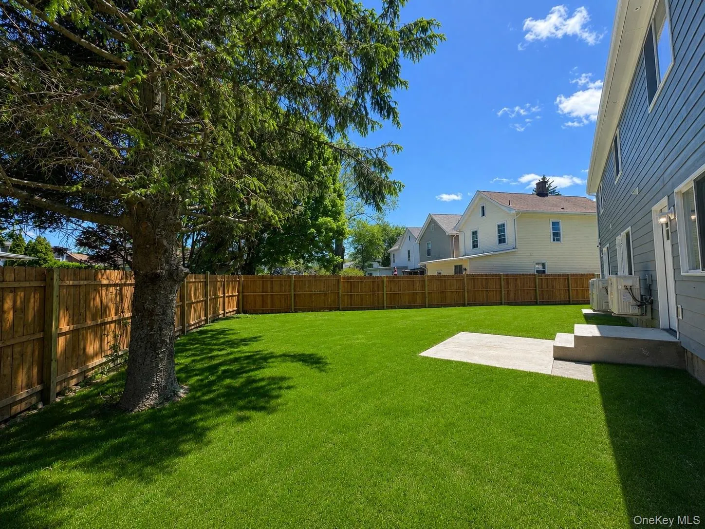 Spacious backyard featuring a manicured lawn, full privacy fencing, and a mature evergreen tree Spacious backyard featuring a manicured lawn, full privacy fencing, and a mature evergreen tree