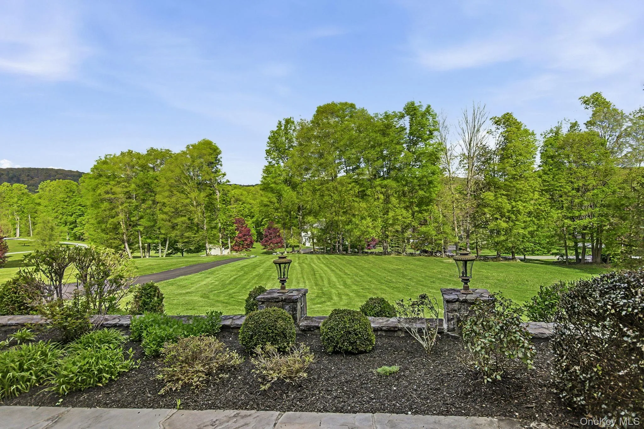 Manicured lawn framed by mature trees, stone-clad light pillars, and landscaped shrubbery Manicured lawn framed by mature trees, stone-clad light pillars, and landscaped shrubbery