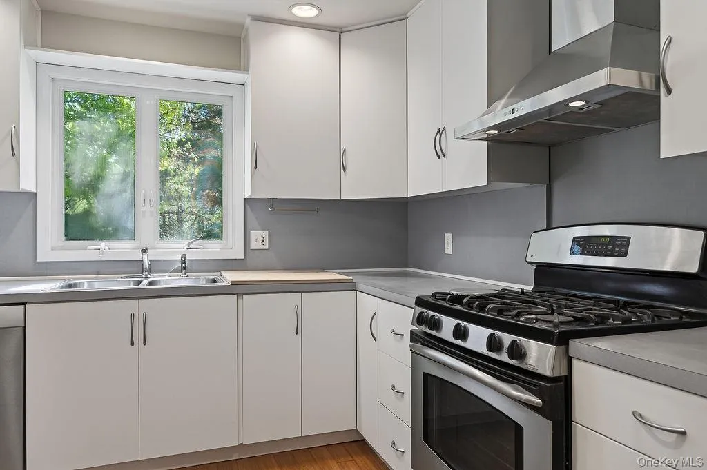 This modern kitchen features white cabinetry, stainless steel appliances, a double basin sink, and wood-finish flooring This modern kitchen features white cabinetry, stainless steel appliances, a double basin sink, and wood-finish flooring