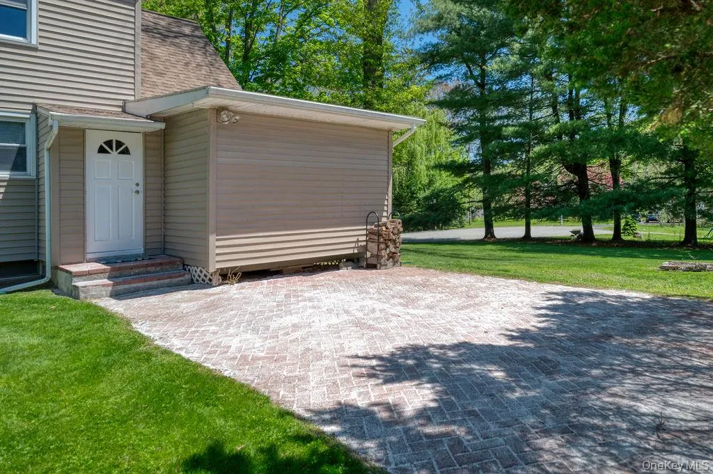 Paver patio featuring a side entry door with fanlight window, extending to a grassy yard with mature trees Paver patio featuring a side entry door with fanlight window, extending to a grassy yard with mature trees