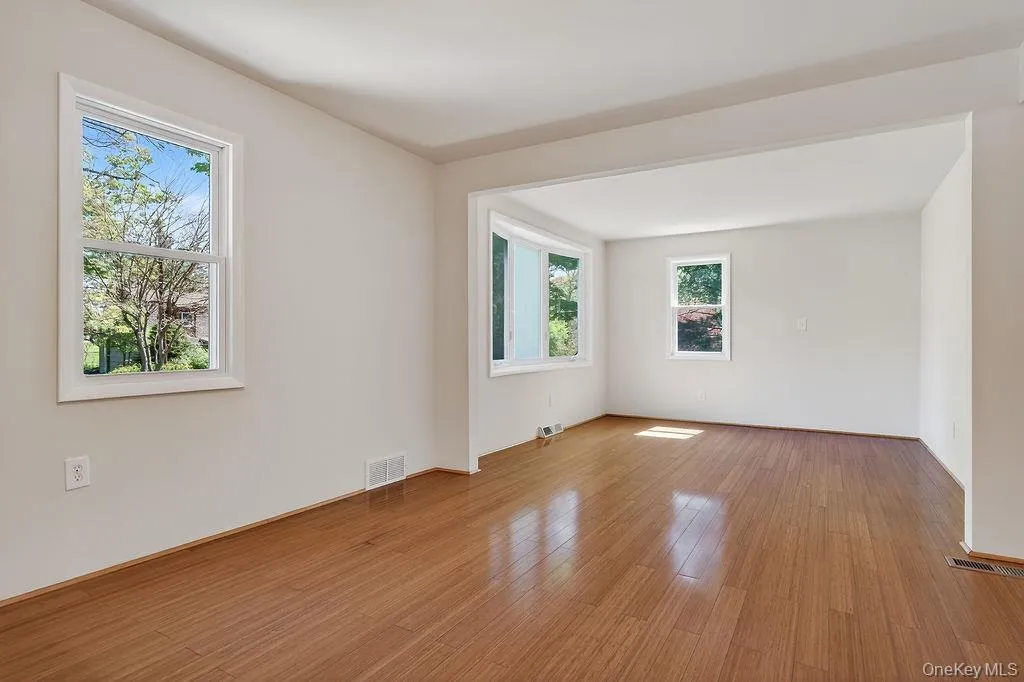 Bright interior with wood-finish flooring, freshly painted walls, multiple windows, a prominent bay window, and a recessed archway Bright interior with wood-finish flooring, freshly painted walls, multiple windows, a prominent bay window, and a recessed archway