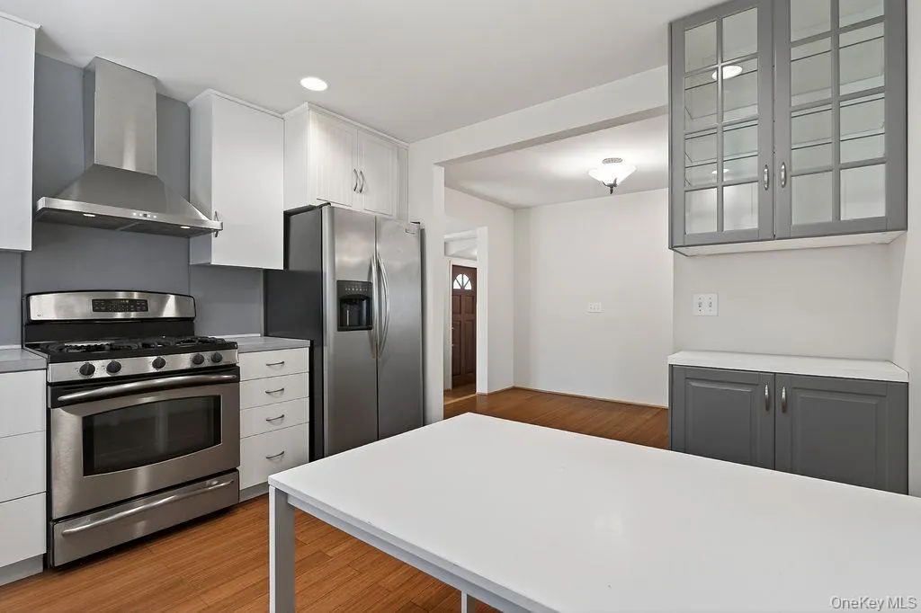 Modern kitchen featuring stainless steel appliances, a range hood, white cabinetry, and wood-finish flooring Modern kitchen featuring stainless steel appliances, a range hood, white cabinetry, and wood-finish flooring