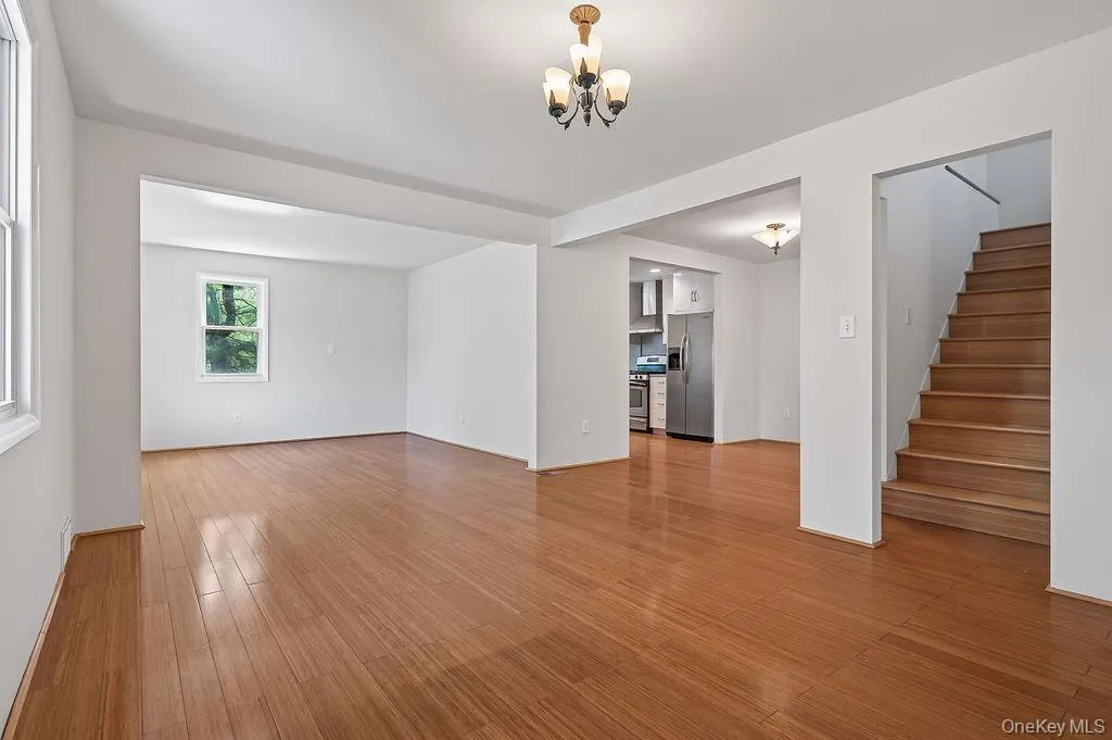 Spacious interior featuring wood-finish bamboo flooring throughout, a visible kitchen area with stainless steel appliances, and a staircase with wood treads Spacious interior featuring wood-finish bamboo flooring throughout, a visible kitchen area with stainless steel appliances, and a staircase with wood treads