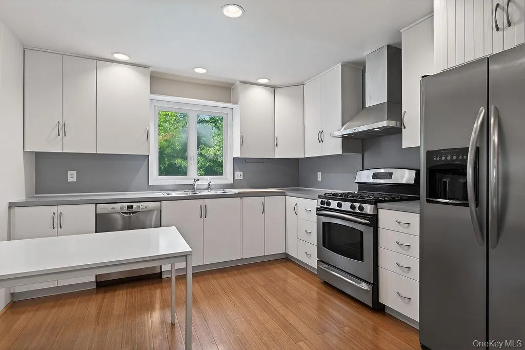 Kitchen featuring stainless steel appliances, wood-finish flooring, white cabinetry, a built-in dishwasher, hood, and recessed lighting. Kitchen featuring stainless steel appliances, wood-finish flooring, white cabinetry, a built-in dishwasher, hood, and recessed lighting.