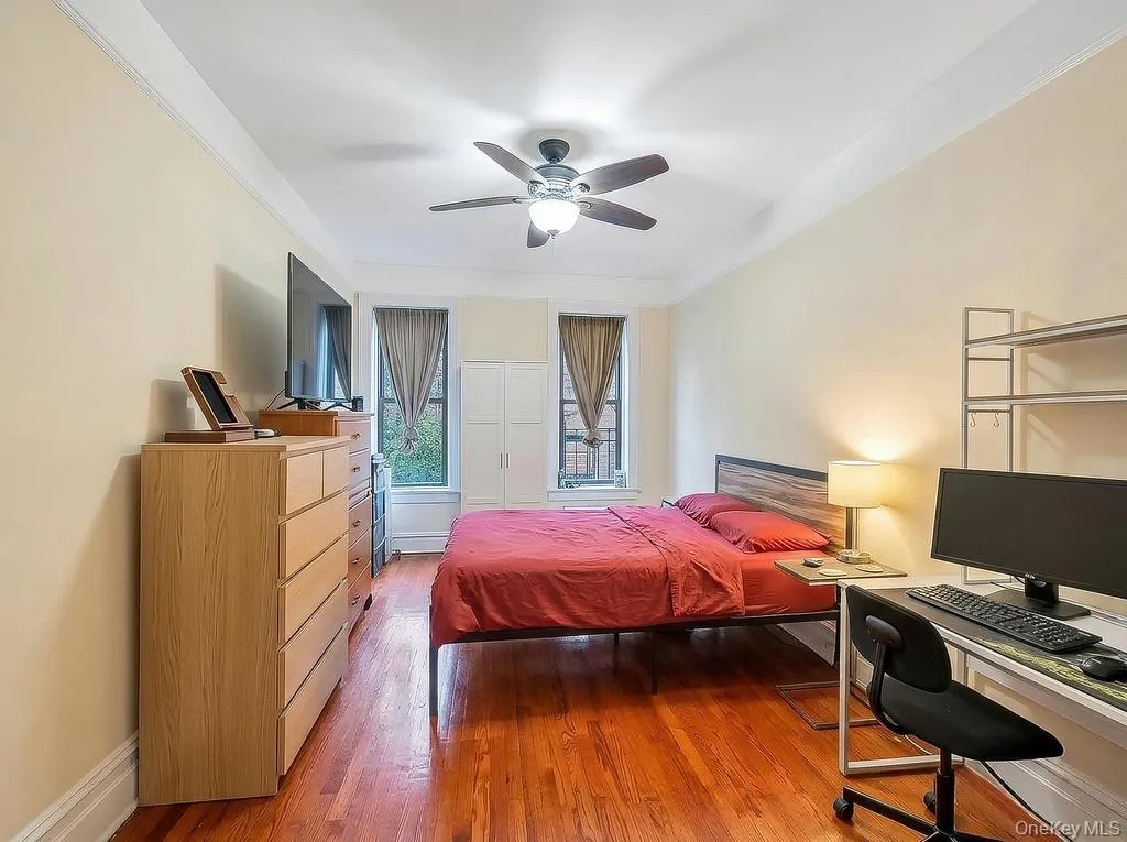 Bedroom featuring wood-finish flooring, two windows with window treatments, a ceiling fan with integrated lighting, and crown molding Bedroom featuring wood-finish flooring, two windows with window treatments, a ceiling fan with integrated lighting, and crown molding