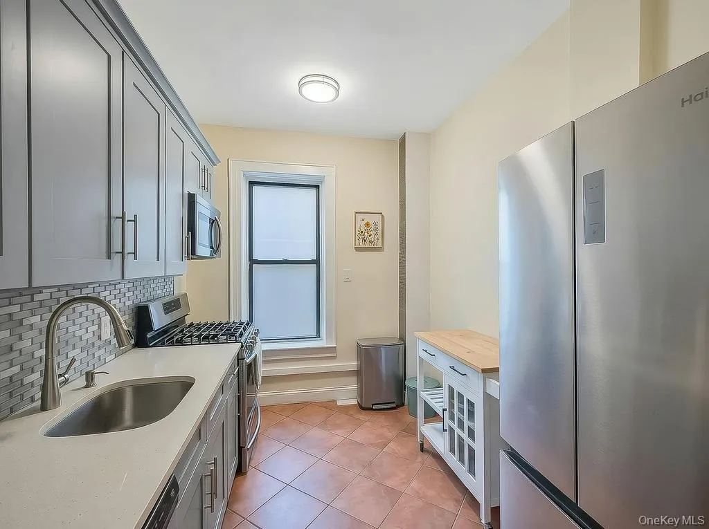 Modern kitchen featuring stainless steel appliances, grey cabinetry, a mosaic tile backsplash, a single-basin sink with a gooseneck faucet, and terracotta-toned floor tile Modern kitchen featuring stainless steel appliances, grey cabinetry, a mosaic tile backsplash, a single-basin sink with a gooseneck faucet, and terracotta-toned floor tile