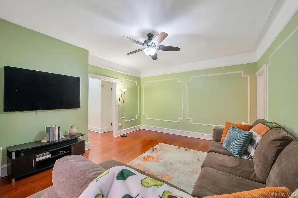 Living area featuring wood-finish flooring, decorative wall molding, a ceiling fan with integrated lighting, and a wide doorway Living area featuring wood-finish flooring, decorative wall molding, a ceiling fan with integrated lighting, and a wide doorway
