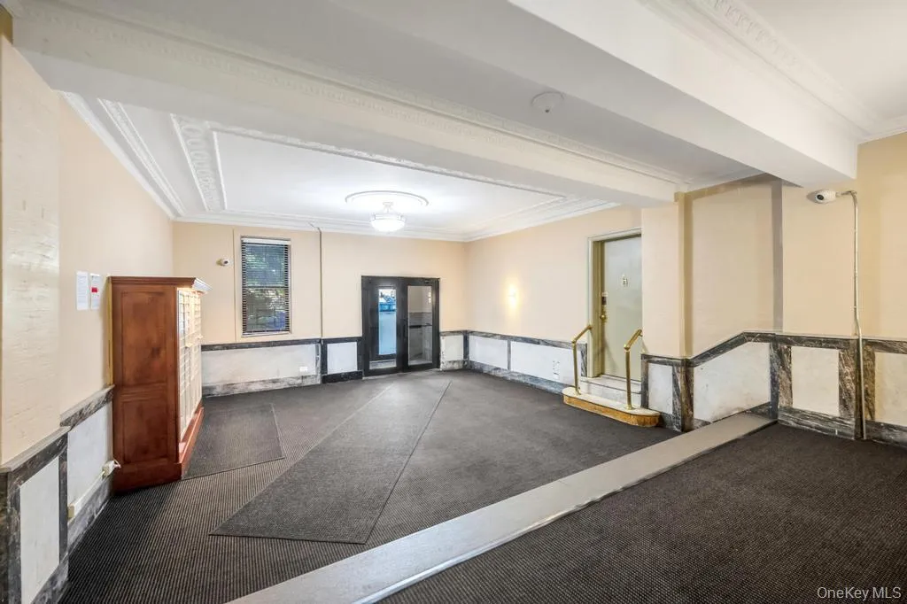 Building entryway featuring patterned ceiling trim, wall sconces, wall-mounted lighting, mixed-material wainscoting, and carpet flooring Building entryway featuring patterned ceiling trim, wall sconces, wall-mounted lighting, mixed-material wainscoting, and carpet flooring