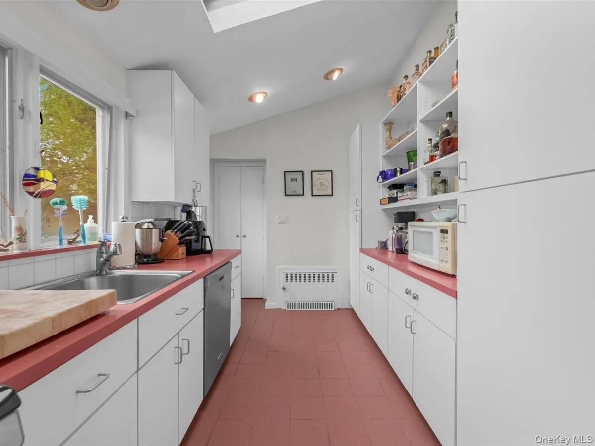 Galley kitchen featuring white cabinetry, red countertops, and a skylight. Stainless Steel Appliances Galley kitchen featuring white cabinetry, red countertops, and a skylight. Stainless Steel Appliances