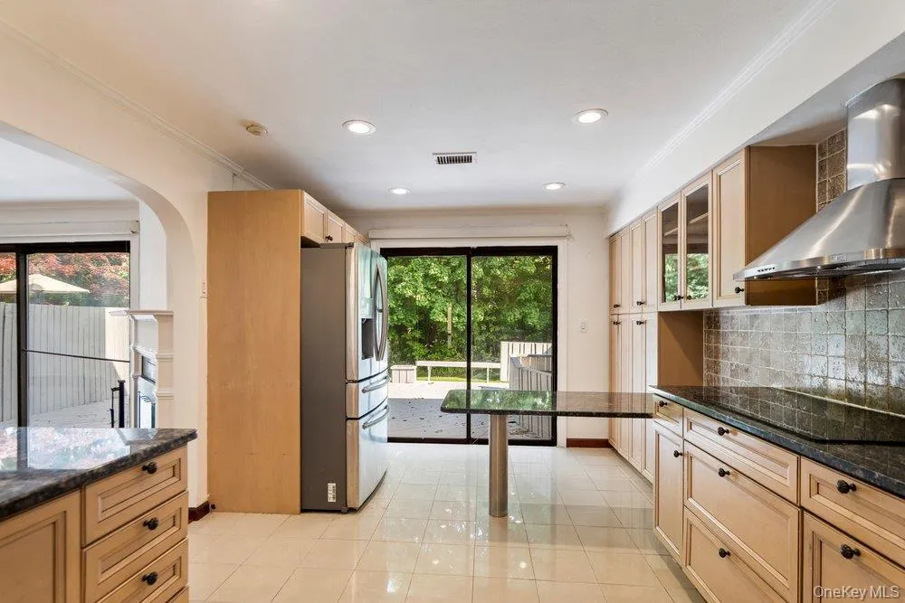 Kitchen featuring light-toned cabinetry, dark granite countertops, stainless steel appliances, and a tiled backsplash Kitchen featuring light-toned cabinetry, dark granite countertops, stainless steel appliances, and a tiled backsplash