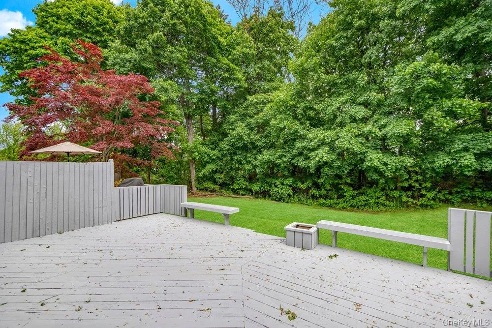 Expansive outdoor deck space featuring painted wood decking, built-in benches, and a planter, with a backdrop of mature trees and a manicured lawn Expansive outdoor deck space featuring painted wood decking, built-in benches, and a planter, with a backdrop of mature trees and a manicured lawn