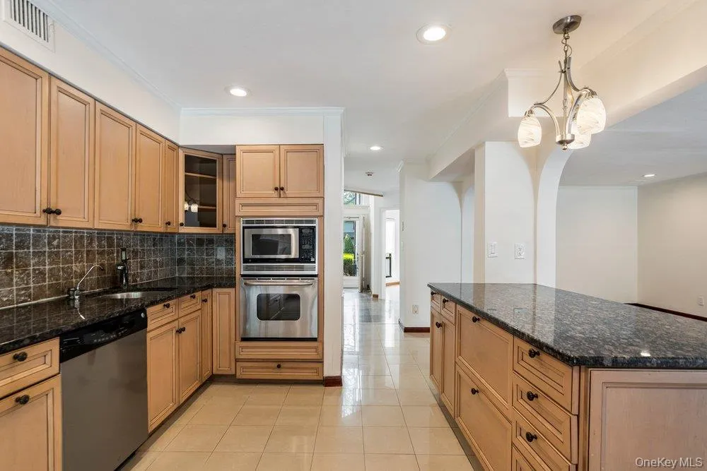 Kitchen featuring wood-finish cabinetry, granite countertops, tile backsplash, and integrated stainless steel appliances including a wall oven and microwave Kitchen featuring wood-finish cabinetry, granite countertops, tile backsplash, and integrated stainless steel appliances including a wall oven and microwave
