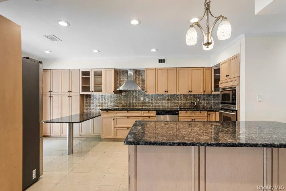 Kitchen featuring an expansive island with a dark stone countertop, light wood cabinetry, recessed lighting, and tile flooring Kitchen featuring an expansive island with a dark stone countertop, light wood cabinetry, recessed lighting, and tile flooring
