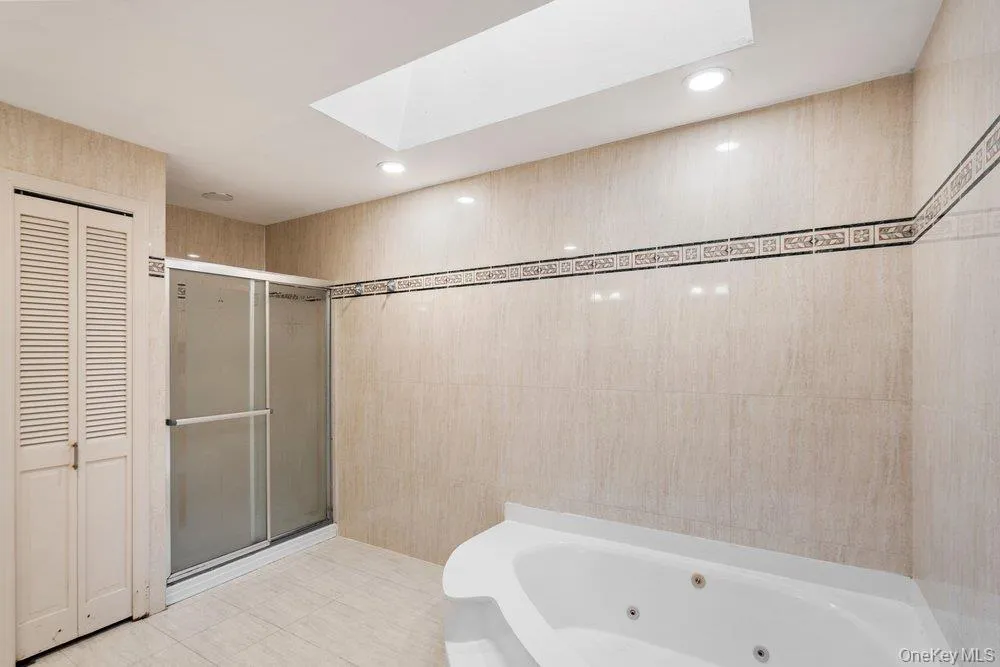 Bathroom featuring a built-in jetted tub, a glass-enclosed shower, a skylight, recessed lighting, and louvered bifold doors Bathroom featuring a built-in jetted tub, a glass-enclosed shower, a skylight, recessed lighting, and louvered bifold doors