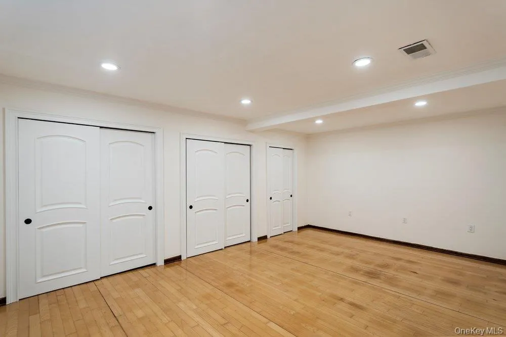 Room featuring wood-finish flooring, recessed lighting, crown molding, and multiple double-door closets with black hardware Room featuring wood-finish flooring, recessed lighting, crown molding, and multiple double-door closets with black hardware