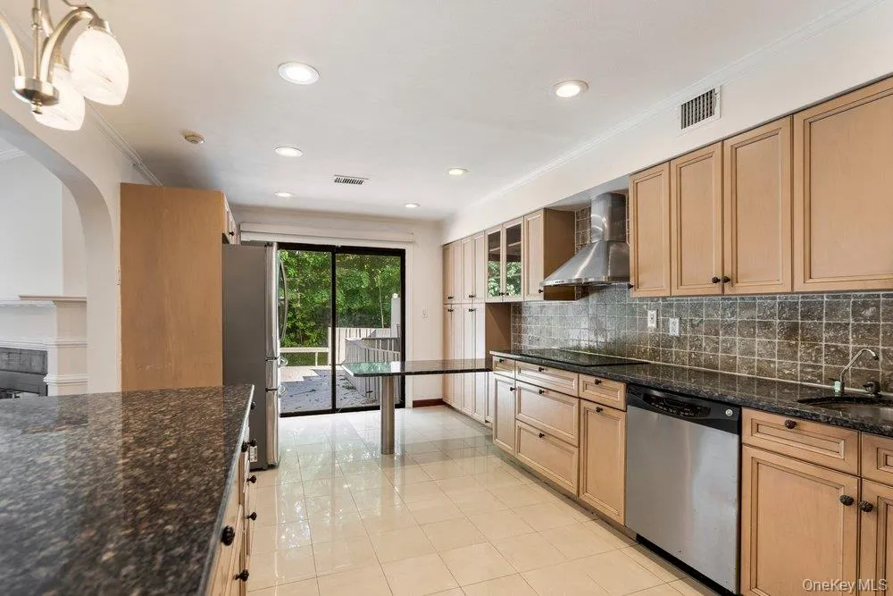 Kitchen featuring wood cabinetry, stainless steel appliances, dark stone countertops, tile flooring, and sliding glass doors to the exterior Kitchen featuring wood cabinetry, stainless steel appliances, dark stone countertops, tile flooring, and sliding glass doors to the exterior