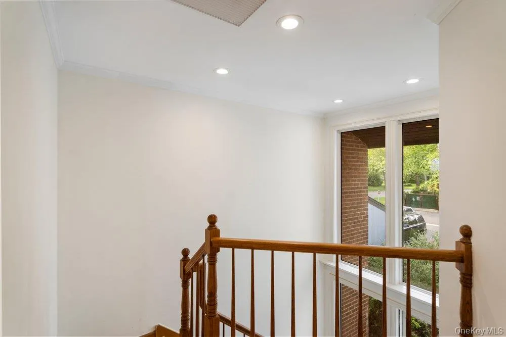 Stairwell featuring a wood-finish banister, crown molding, recessed lighting, and a large window with white trim Stairwell featuring a wood-finish banister, crown molding, recessed lighting, and a large window with white trim