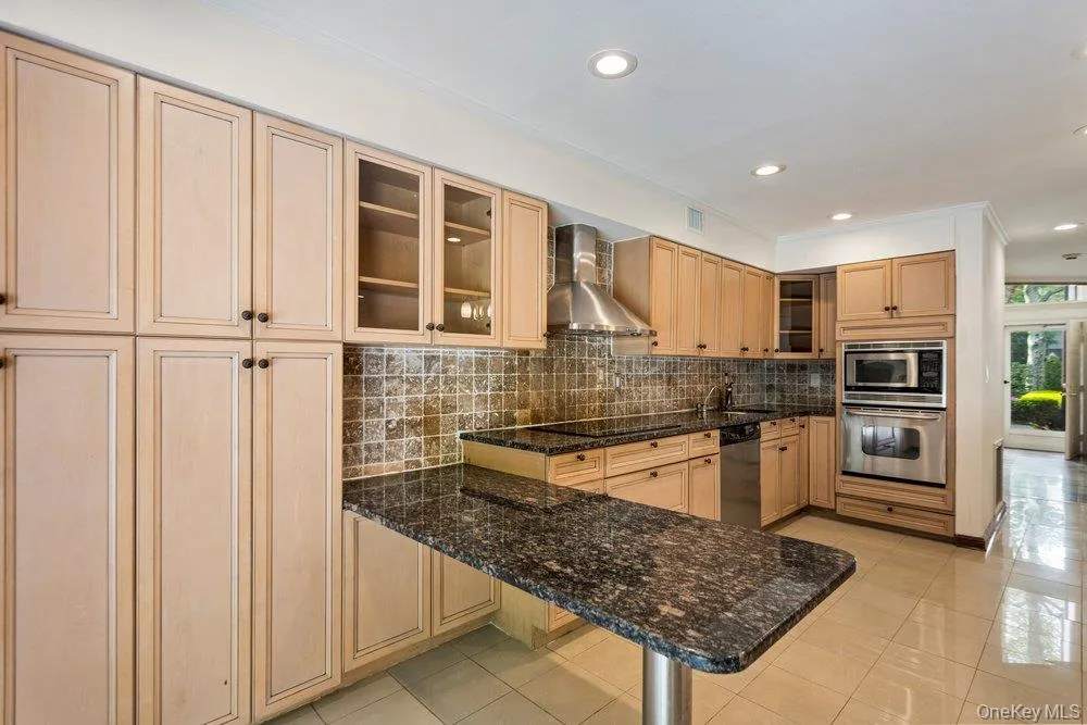 Kitchen featuring extensive light wood cabinetry, stone-finish countertops, and a tiled backsplash Kitchen featuring extensive light wood cabinetry, stone-finish countertops, and a tiled backsplash