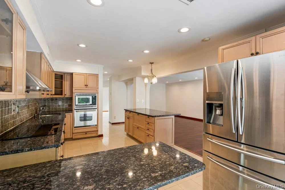 Spacious kitchen featuring granite countertops, light wood cabinetry, stainless steel appliances including a double oven and refrigerator, and recessed lighting Spacious kitchen featuring granite countertops, light wood cabinetry, stainless steel appliances including a double oven and refrigerator, and recessed lighting