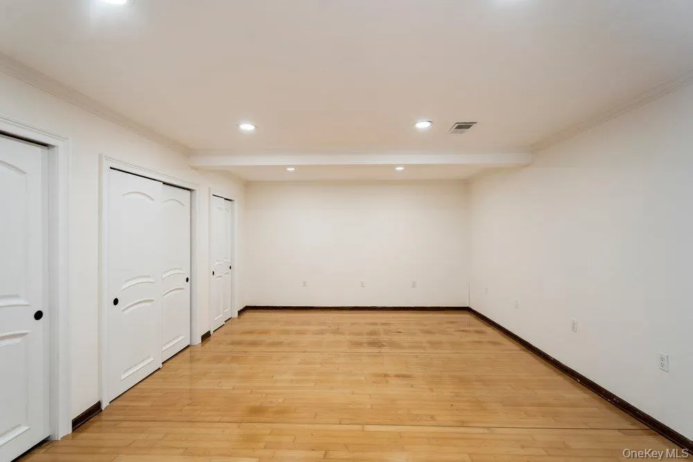 Spacious room featuring wood-finish flooring, recessed lighting, and multiple white panel doors Spacious room featuring wood-finish flooring, recessed lighting, and multiple white panel doors