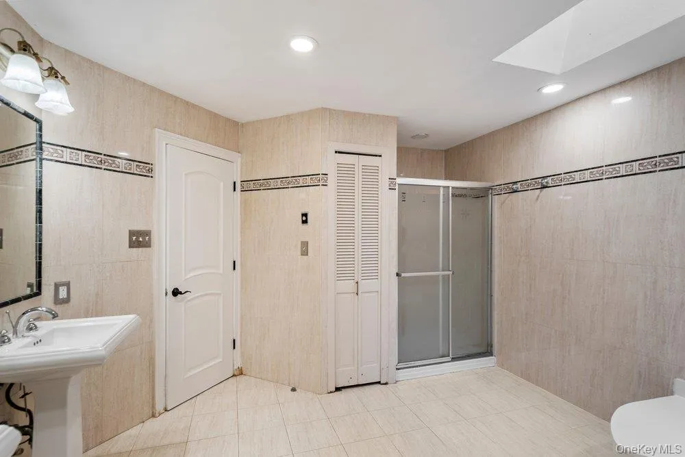 Tiled bathroom featuring a pedestal sink, framed mirror, and a glass-enclosed shower Tiled bathroom featuring a pedestal sink, framed mirror, and a glass-enclosed shower