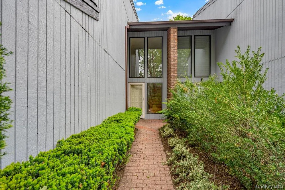 Brick pathway entry framed by manicured hedges and established shrubs, leading to a recessed entryway with a full-light door Brick pathway entry framed by manicured hedges and established shrubs, leading to a recessed entryway with a full-light door