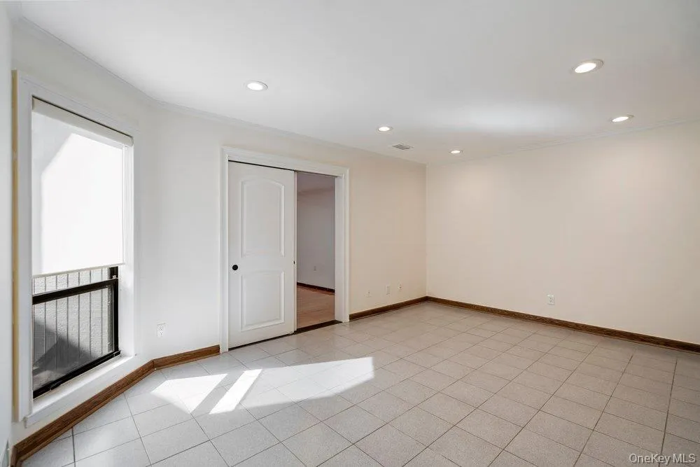 Bright room featuring light-toned tile flooring, recessed ceiling lighting, and a window with a roller shade Bright room featuring light-toned tile flooring, recessed ceiling lighting, and a window with a roller shade