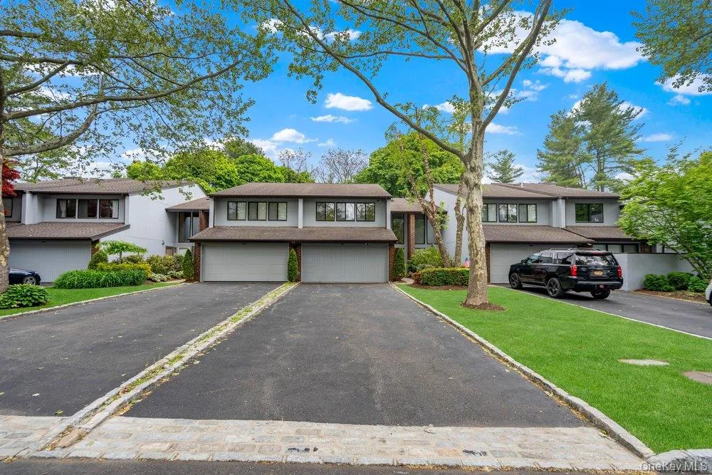 Contemporary multi-level residence featuring a two-car garage, asphalt driveway, mature tree landscaping, and a manicured lawn Contemporary multi-level residence featuring a two-car garage, asphalt driveway, mature tree landscaping, and a manicured lawn