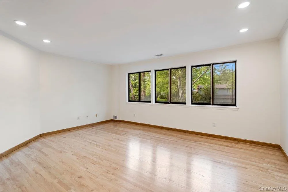 Spacious room featuring light wood-finish flooring, recessed ceiling lighting, and multiple windows providing ample natural light Spacious room featuring light wood-finish flooring, recessed ceiling lighting, and multiple windows providing ample natural light