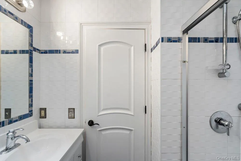 Bathroom featuring white tiled walls with a blue accent band, a glass-enclosed shower, and a vanity with an integrated sink and chrome faucet Bathroom featuring white tiled walls with a blue accent band, a glass-enclosed shower, and a vanity with an integrated sink and chrome faucet