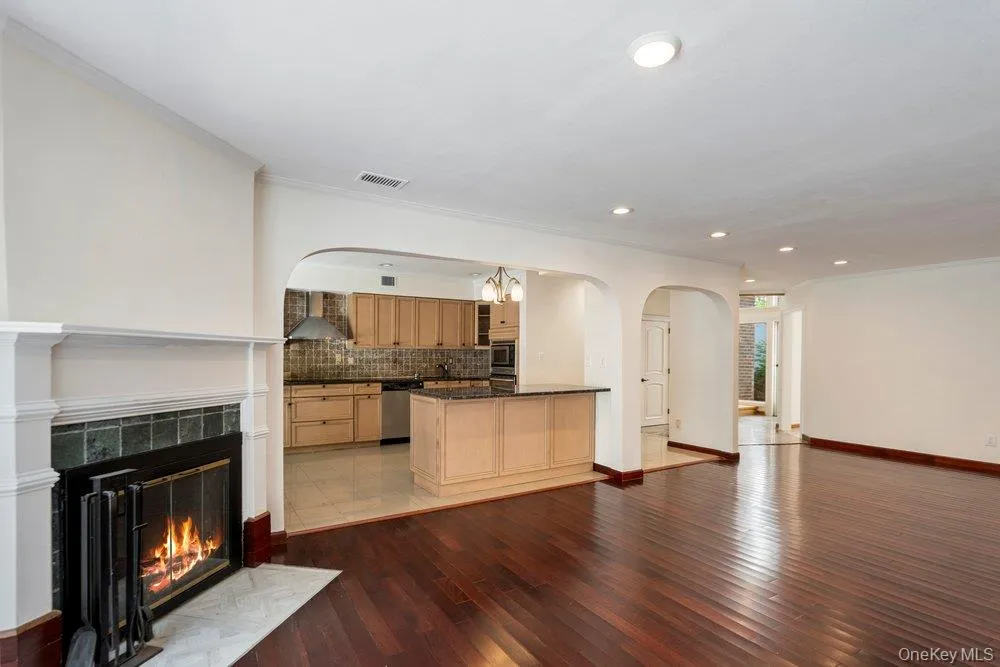 Spacious interior showcasing rich wood-finish flooring, a classic fireplace with a detailed mantel and tile surround, and recessed lighting Spacious interior showcasing rich wood-finish flooring, a classic fireplace with a detailed mantel and tile surround, and recessed lighting