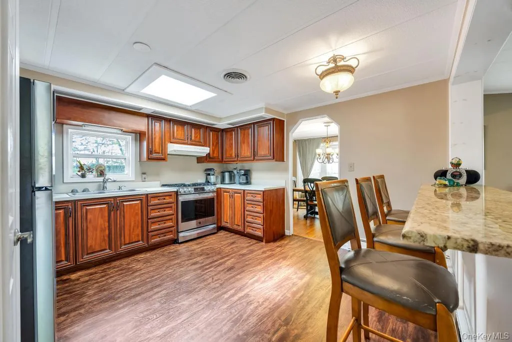 Kitchen featuring wood-finish flooring, rich wood cabinetry, stainless steel appliances, and a skylight Kitchen featuring wood-finish flooring, rich wood cabinetry, stainless steel appliances, and a skylight
