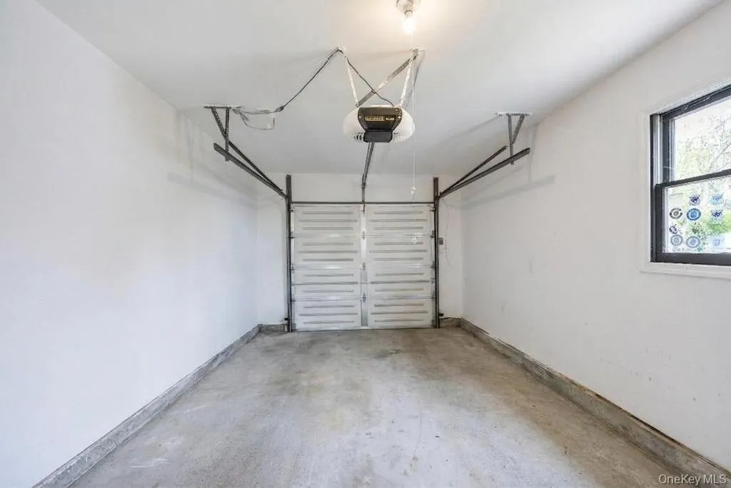 Attached garage space featuring concrete flooring, a single overhead door, and a built-in window with black trim Attached garage space featuring concrete flooring, a single overhead door, and a built-in window with black trim