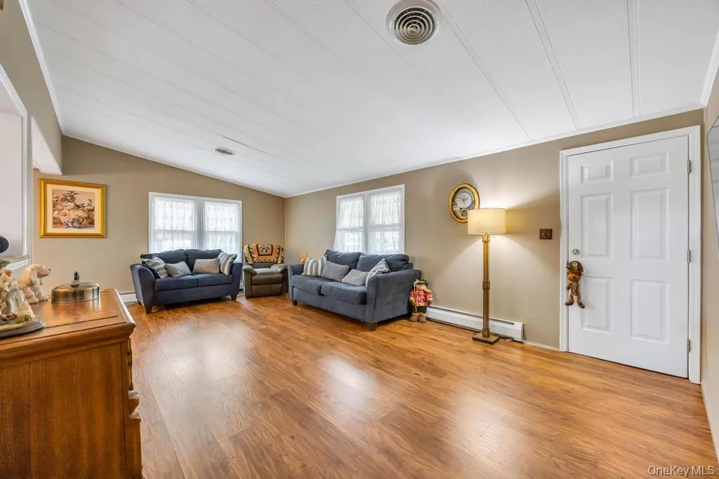 Spacious living area featuring wood-finish flooring, a vaulted ceiling with white paneling, and neutral wall tones Spacious living area featuring wood-finish flooring, a vaulted ceiling with white paneling, and neutral wall tones