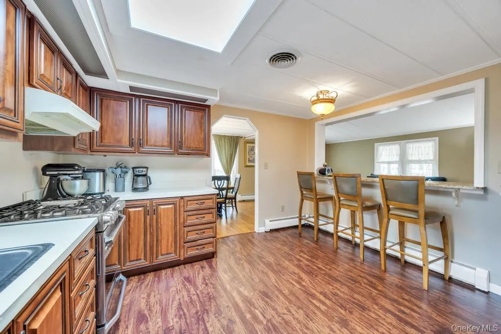 Kitchen featuring wood-finish flooring, warm wood cabinetry, light countertops, and a skylight Kitchen featuring wood-finish flooring, warm wood cabinetry, light countertops, and a skylight