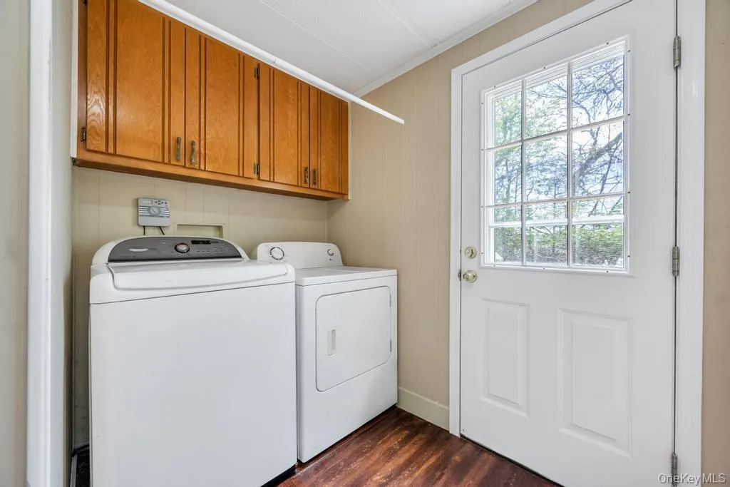 Laundry area featuring wood-finish flooring, overhead wood cabinetry, and a white paneled door with grid-patterned glass Laundry area featuring wood-finish flooring, overhead wood cabinetry, and a white paneled door with grid-patterned glass
