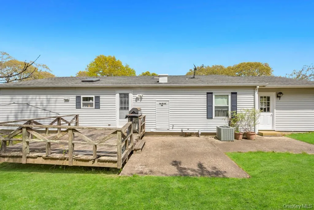 Rear exterior featuring a wooden deck with railing, a concrete patio, and a white siding facade Rear exterior featuring a wooden deck with railing, a concrete patio, and a white siding facade