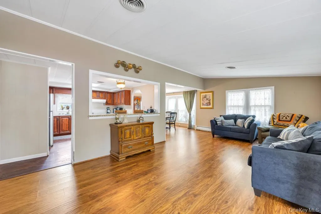 Spacious living area featuring wood-finish flooring, neutral wall tones, and multiple windows with white trim Spacious living area featuring wood-finish flooring, neutral wall tones, and multiple windows with white trim