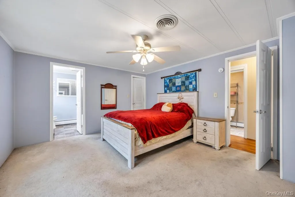 Spacious bedroom featuring light-colored carpeting, a ceiling fan with integrated lighting, and direct access to an attached bathroom with tiled flooring Spacious bedroom featuring light-colored carpeting, a ceiling fan with integrated lighting, and direct access to an attached bathroom with tiled flooring