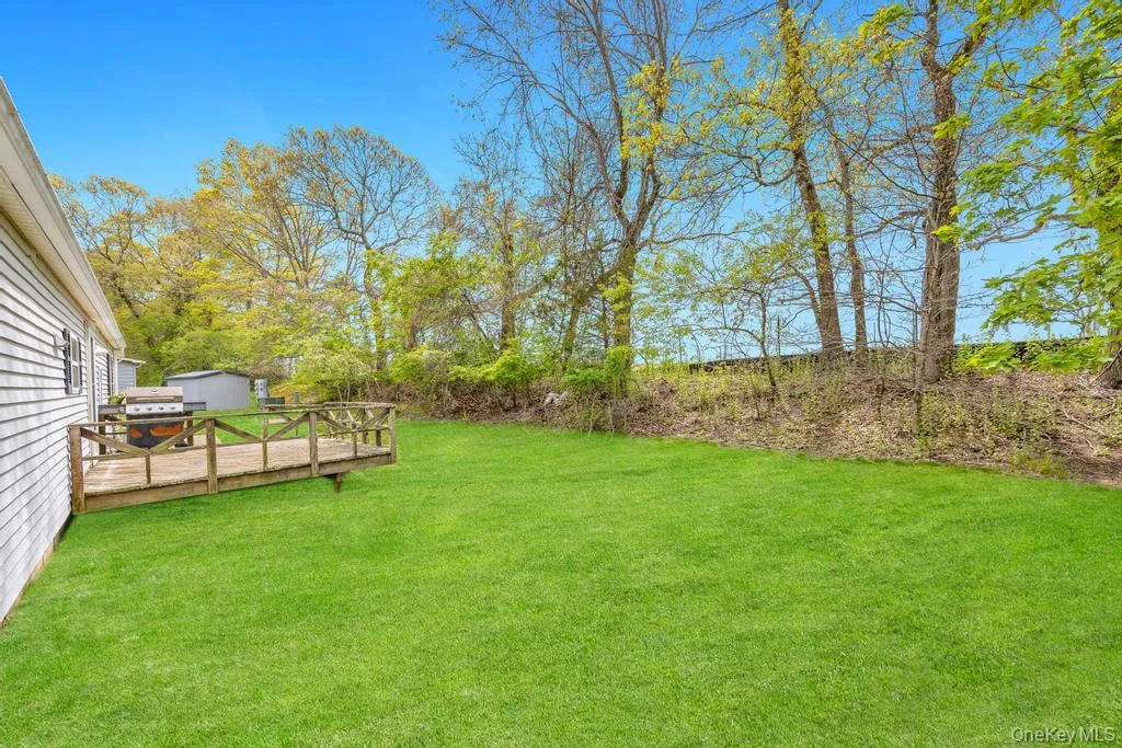Expansive rear yard featuring a wooden deck with railing, a lush green lawn, and mature trees providing natural screening Expansive rear yard featuring a wooden deck with railing, a lush green lawn, and mature trees providing natural screening