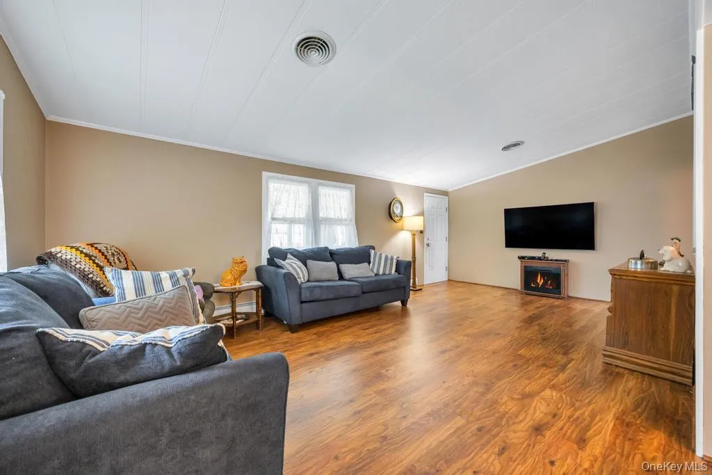 Spacious living area featuring wood-finish flooring, neutral wall tones, and crown molding Spacious living area featuring wood-finish flooring, neutral wall tones, and crown molding