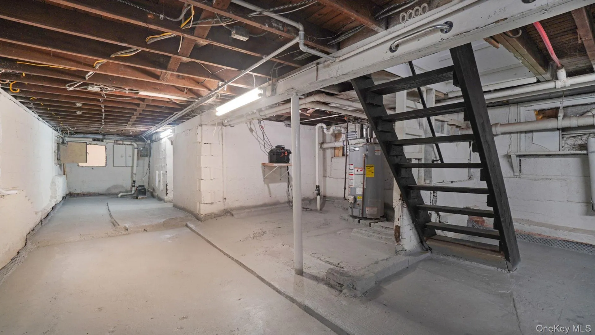 Unfinished below grade area featuring water heater and stairs Unfinished below grade area featuring water heater and stairs