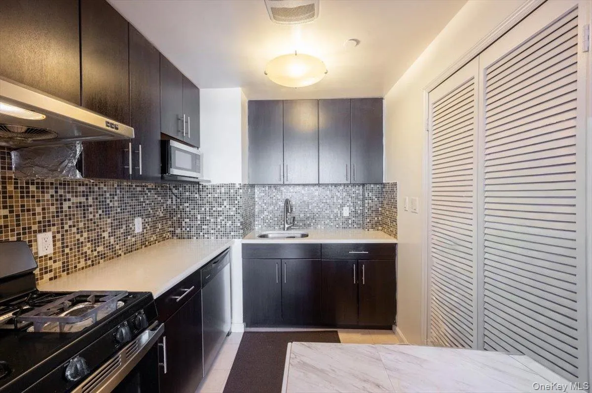Kitchen with appliances with stainless steel finishes, decorative backsplash, light stone counters, and under cabinet range hood Kitchen with appliances with stainless steel finishes, decorative backsplash, light stone counters, and under cabinet range hood