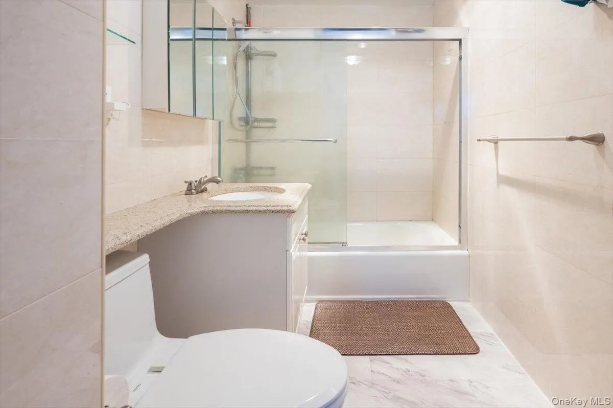 Full bath featuring vanity, tile walls, and combined bath / shower with glass door Full bath featuring vanity, tile walls, and combined bath / shower with glass door