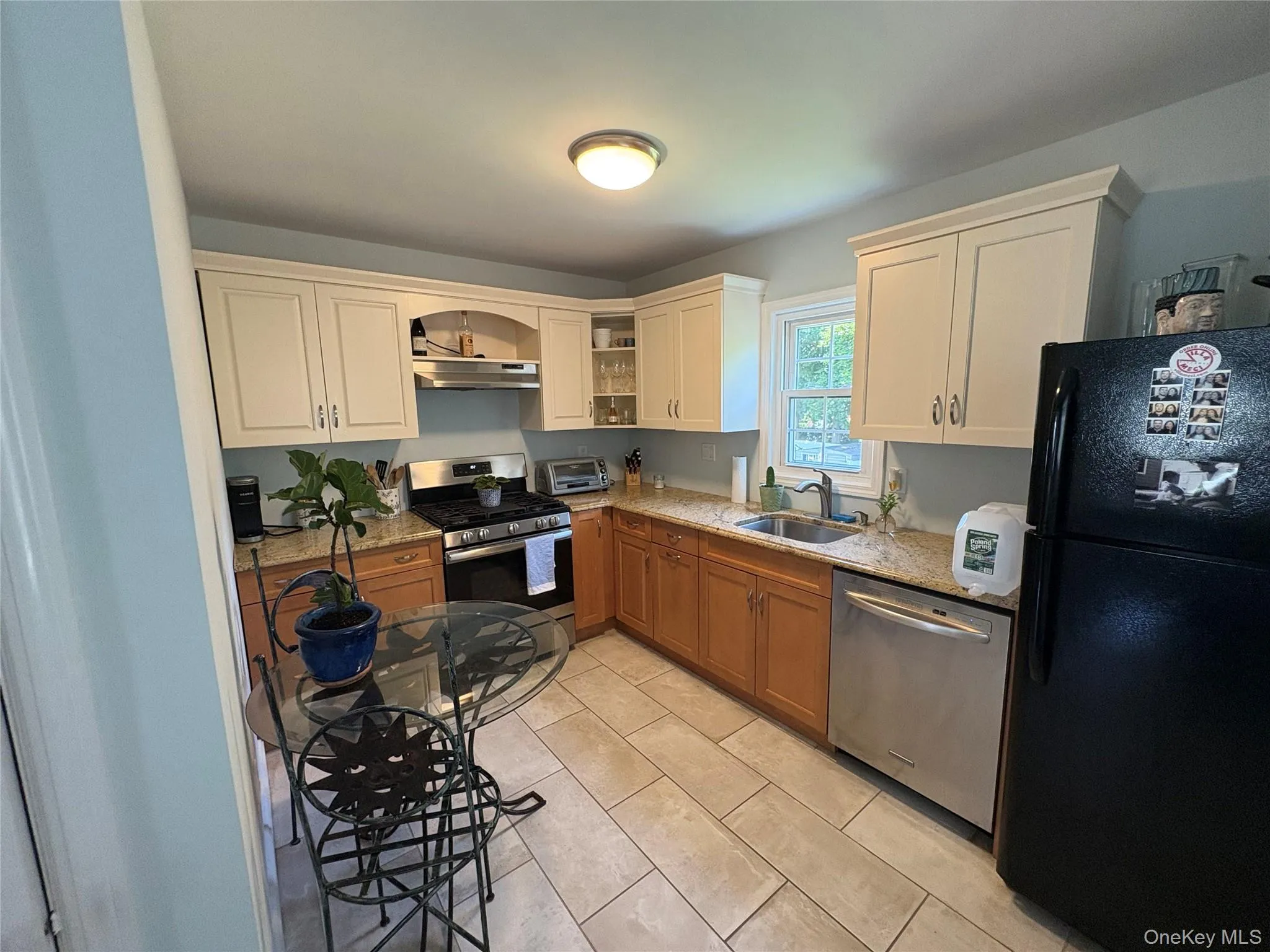 Kitchen featuring appliances with stainless steel finishes, exhaust hood, light stone countertops, open shelves, and light tile patterned floors Kitchen featuring appliances with stainless steel finishes, exhaust hood, light stone countertops, open shelves, and light tile patterned floors
