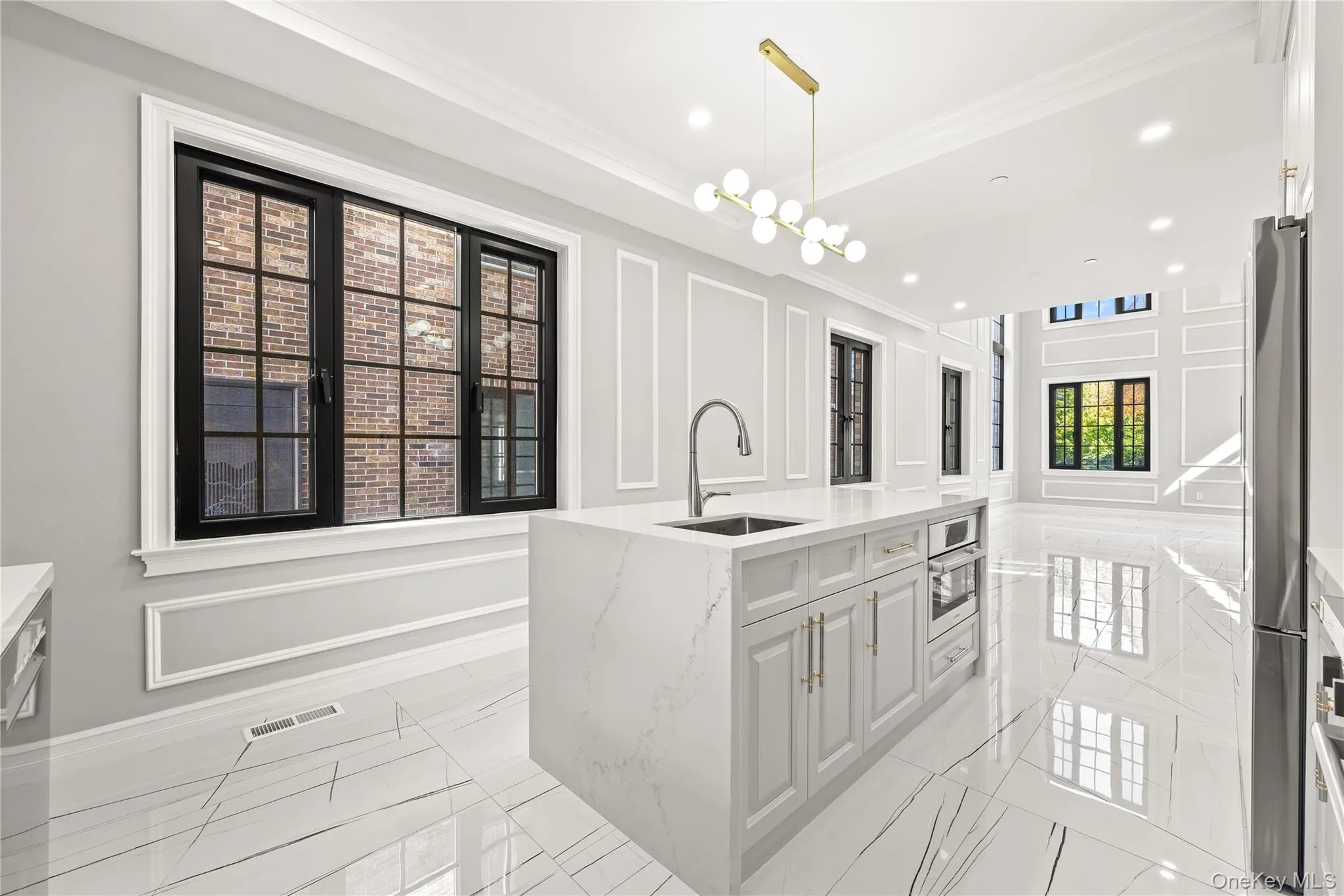 Kitchen with a decorative wall, pendant lighting, light stone counters, an island with sink, and stainless steel appliances Kitchen with a decorative wall, pendant lighting, light stone counters, an island with sink, and stainless steel appliances