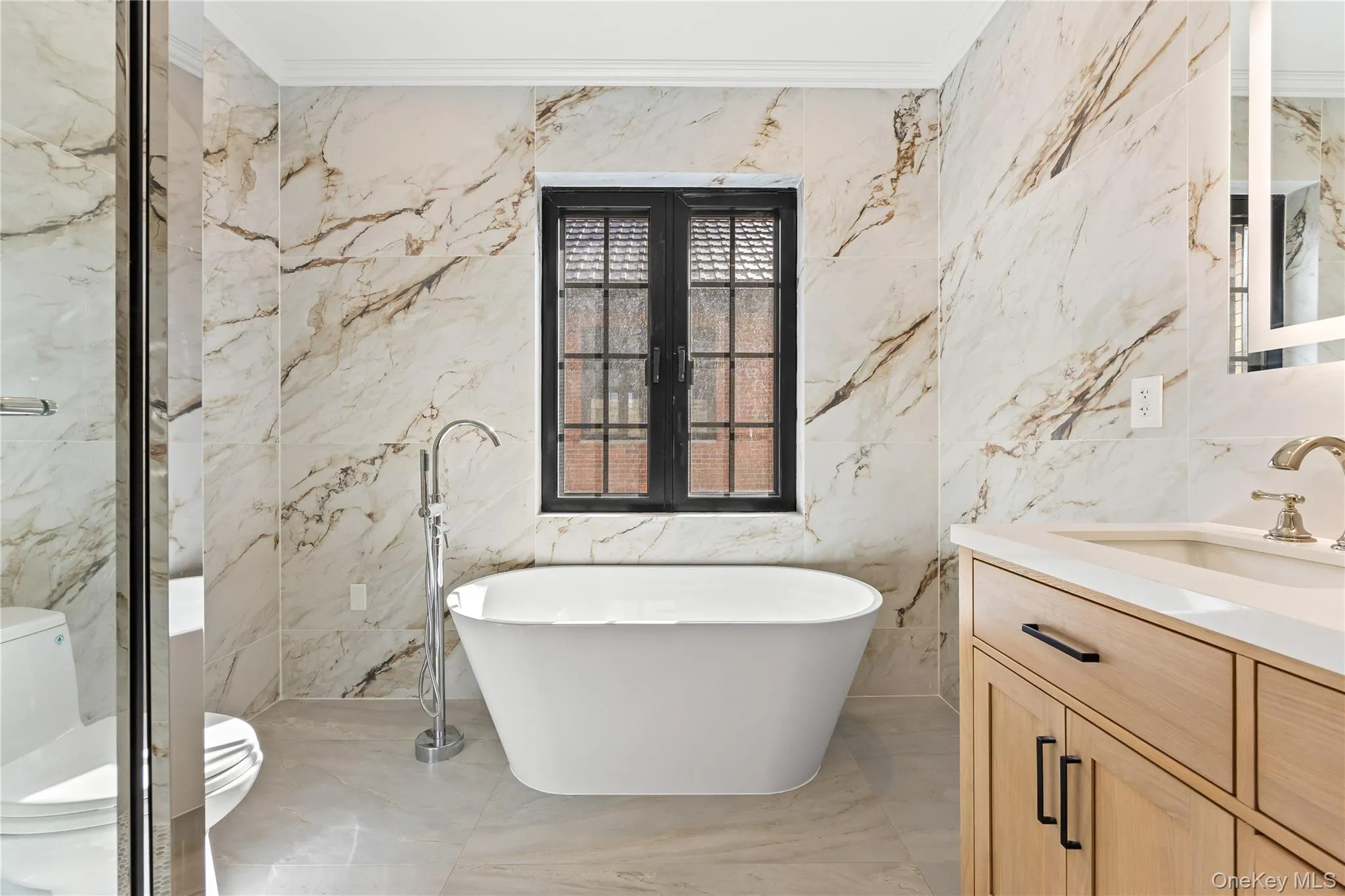 Full bathroom with vanity, a freestanding tub, crown molding, light marble finish floors, and stone wall Full bathroom with vanity, a freestanding tub, crown molding, light marble finish floors, and stone wall