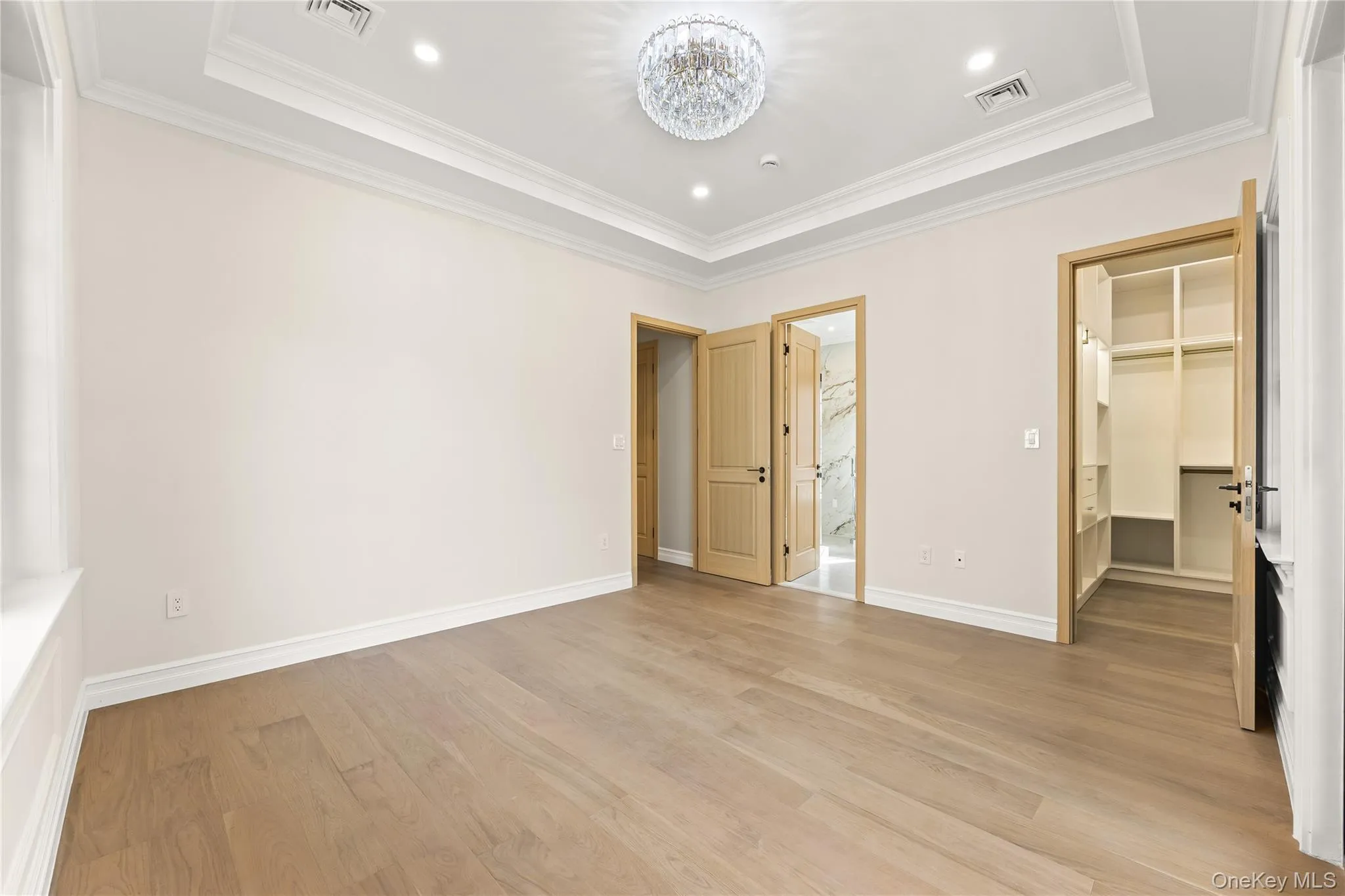 Unfurnished bedroom with a spacious closet, light wood-style floors, a chandelier, a raised ceiling, and recessed lighting Unfurnished bedroom with a spacious closet, light wood-style floors, a chandelier, a raised ceiling, and recessed lighting