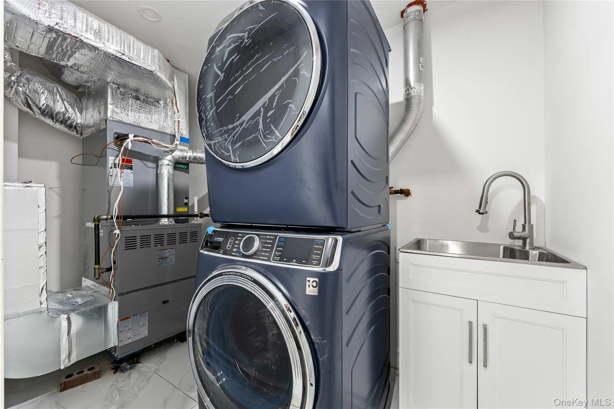 Washroom with stacked washing machine and dryer, heating unit, marble look tiles, and cabinet space Washroom with stacked washing machine and dryer, heating unit, marble look tiles, and cabinet space