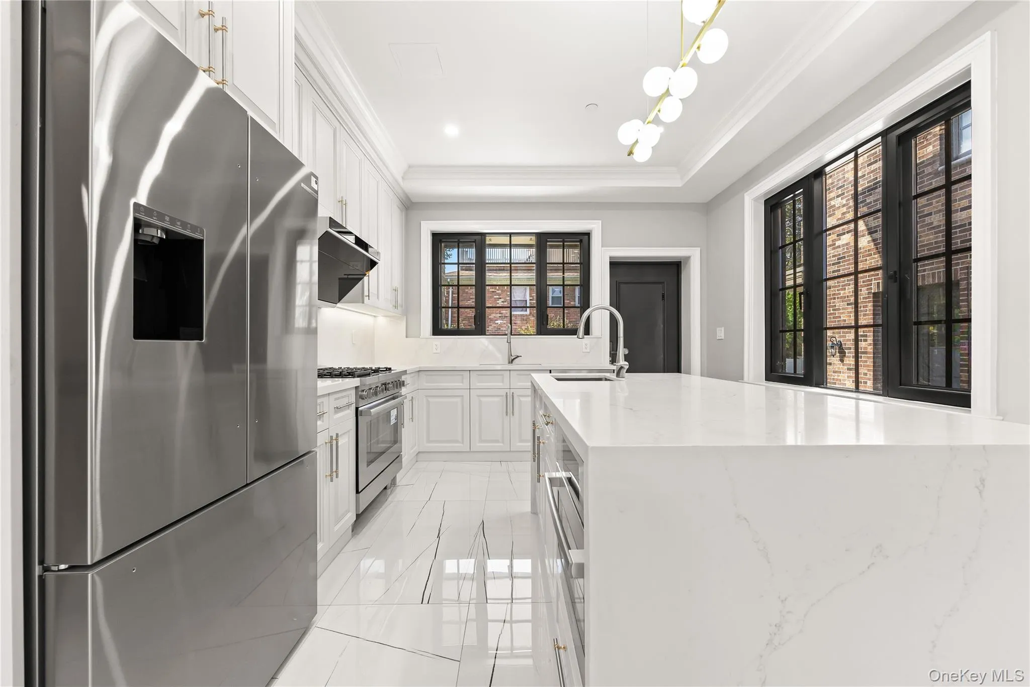 Kitchen featuring stainless steel appliances, white cabinetry, light stone counters, a tray ceiling, and light marble finish floors Kitchen featuring stainless steel appliances, white cabinetry, light stone counters, a tray ceiling, and light marble finish floors
